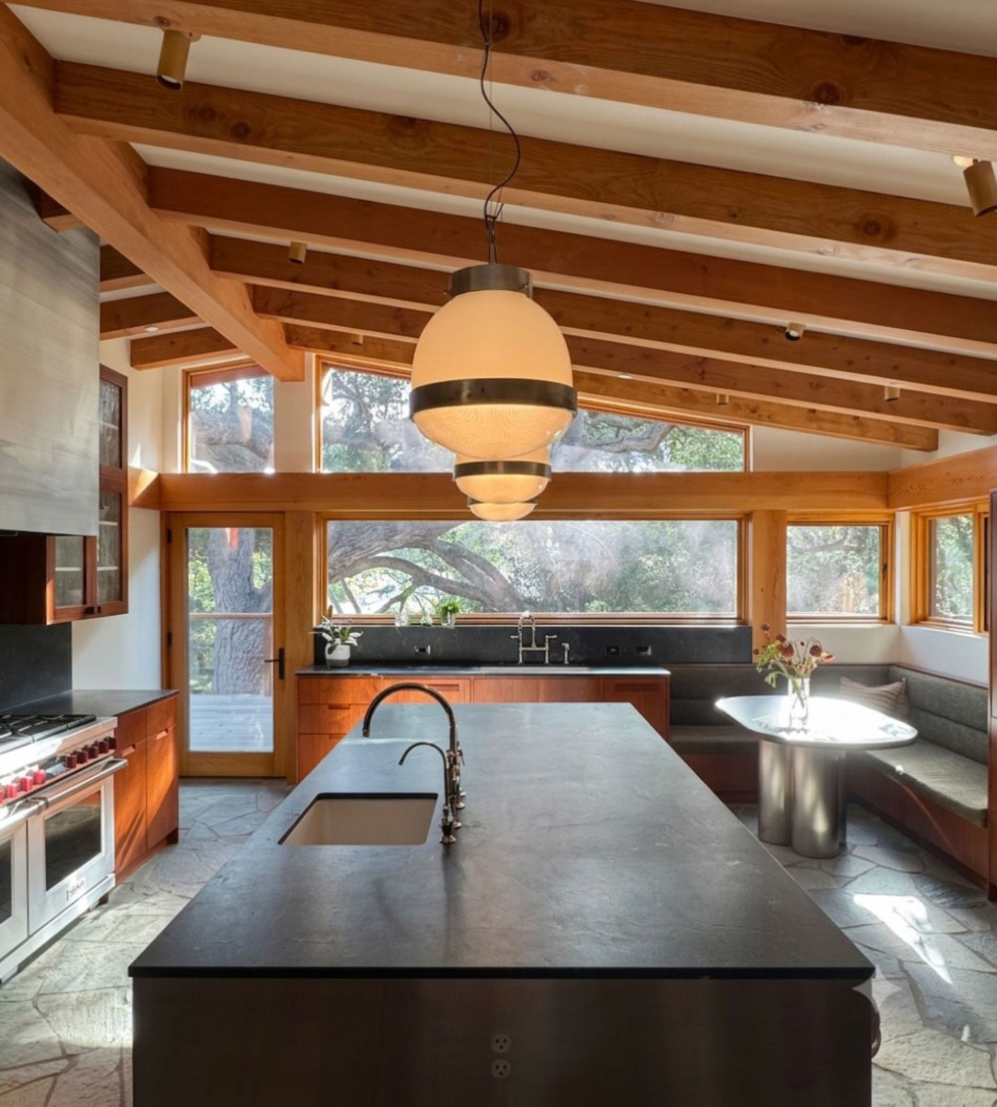 A cedar-beam kitchen with a soapstone island opening to oak trees