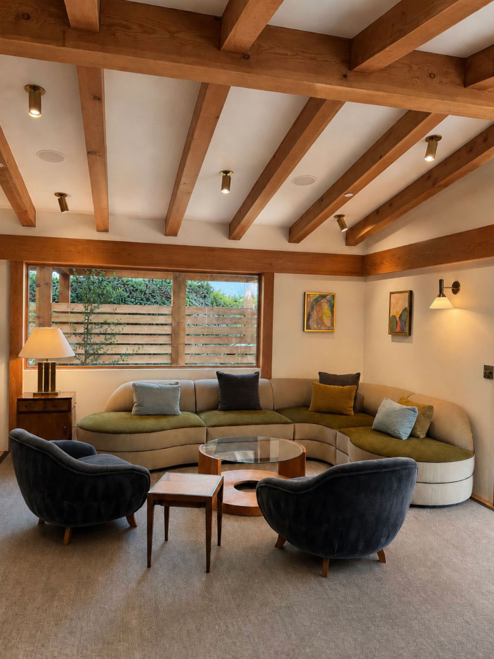 A living room with a curved sofa, velvet chairs, and a beamed cedar ceiling
